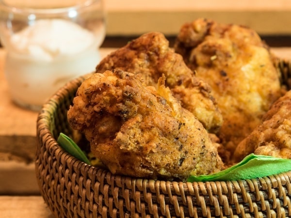 Electric skillet fried chicken in weaved basket with garlic mayo on the side and green napkins.