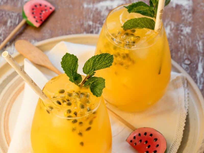 Passion Fruit & Ginger Mojitos in wine glasses with watermelon swizzle sticks.