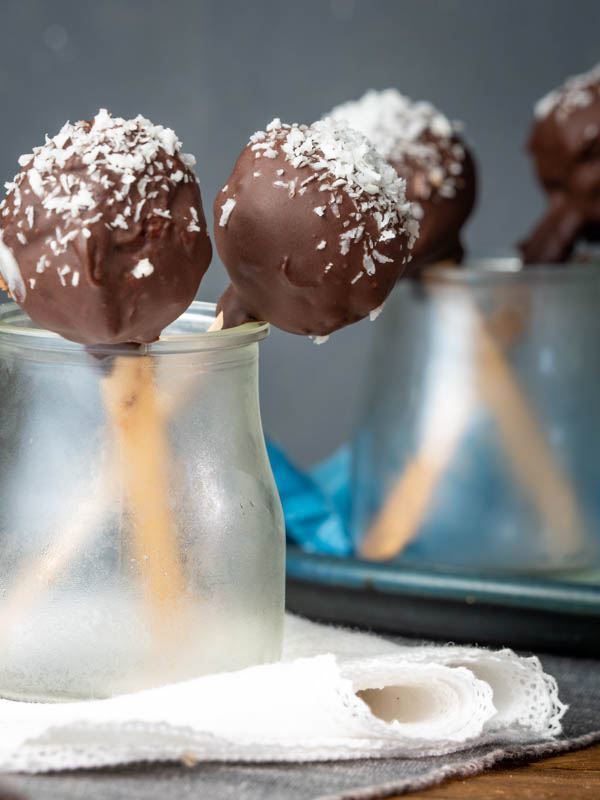 Cheesecake Cake Pops Coated in Dark Chocolate & Coconut Flakes sitting in glass jar on a cloth napkin. inthekitch.net
