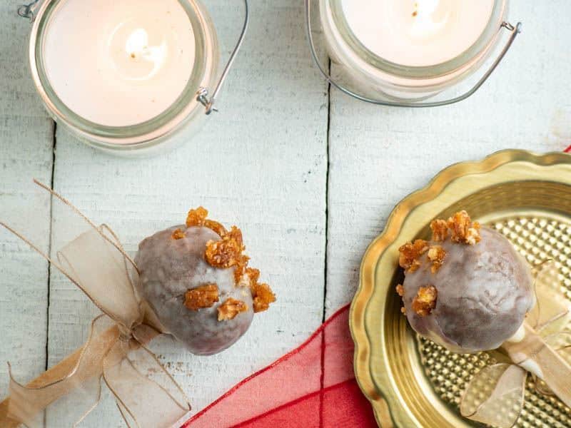 Christmas cake pops on wooden white background with 2 white candles glowing in the background.