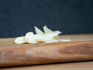 How to Slice Garlic-Step 4 image, sliced garlic on a wooden cutting board. inthekitch.net