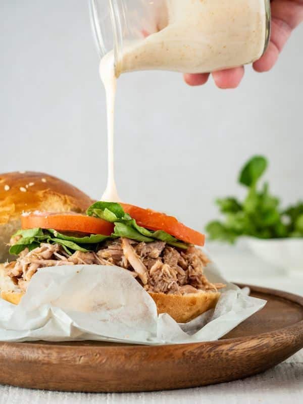 Pulled Pork Burger with Special Sauce drizzling on top on a wooden plate.