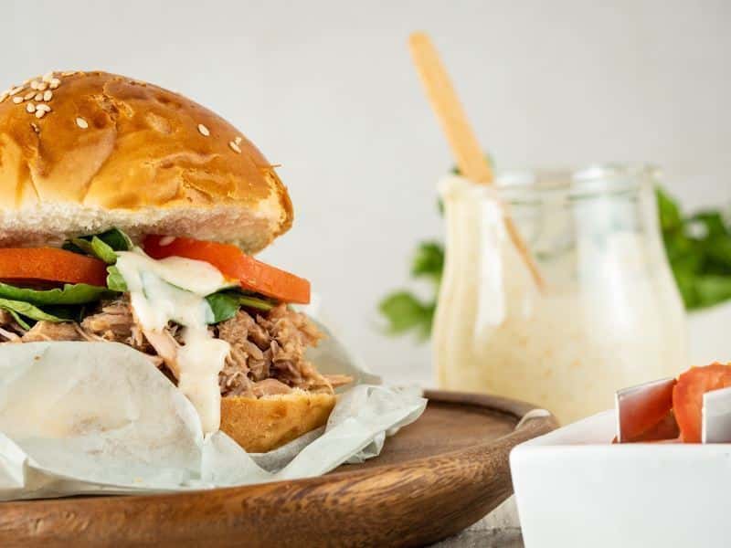 Pulled pork burger on wooden plate with a jar of special sauce in the background.