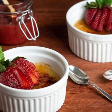 Crème Brûlée with Raspberry Coulis in ramekins with strawberries on top.