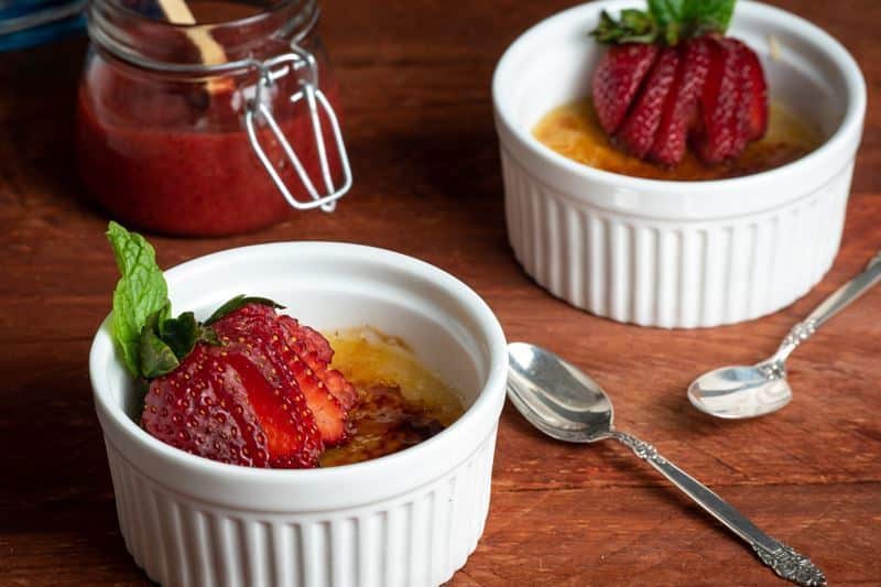 Crème Brûlée with Raspberry Coulis in ramekins with strawberries on top.