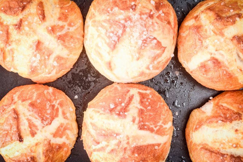 6 pretzel bread rolls layed flat on a pan.