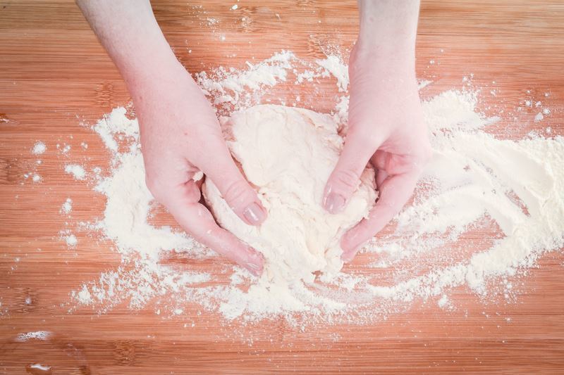 Hands mixing dough on floured surface.