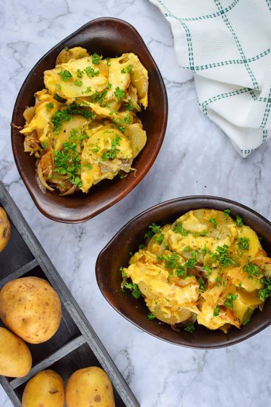 Electric Skillet Scalloped Potatoes in a wooden dish, potatoes in the background.