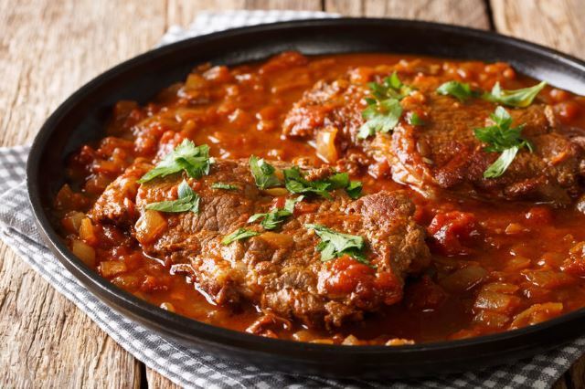 Skillet Swiss Steak on black plate, wood background.