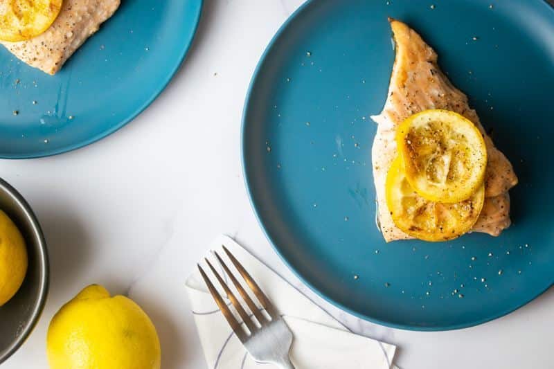 How to Cook Salmon With Skin Step 8-8 Cooked salmon with grilled lemon slices on plates and lemons on the table.