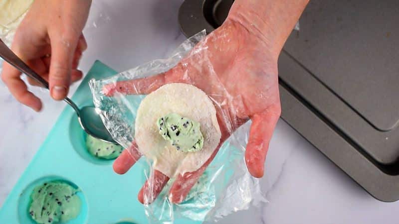 Woman's hand holding mochi dough circle with a portion of ice cream in it.