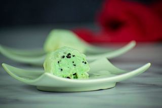 Mint green mochi ice cream that has been cut open, on a mint-colored dish.
