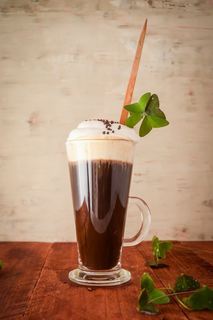 Irish Coffee with a four-leaf clover on light brown background.
