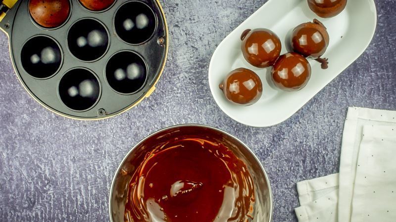 Cake pop maker, bowl of melted chocolate coating and dish of chocolate covered donut holes.