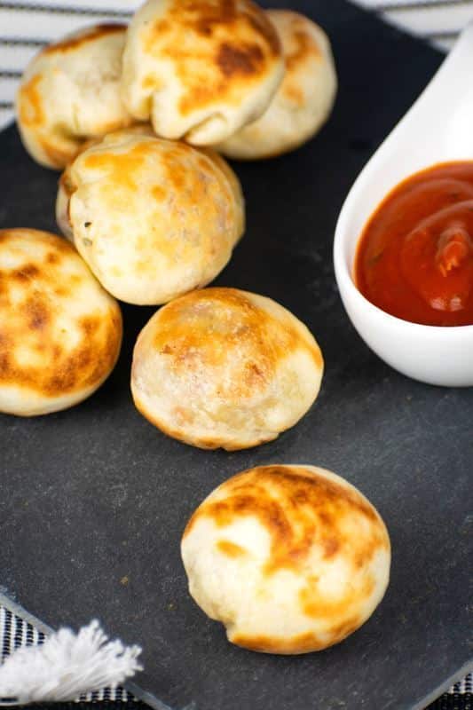 Pizza balls on a black serving plate, small dish of marinara sauce on the side.