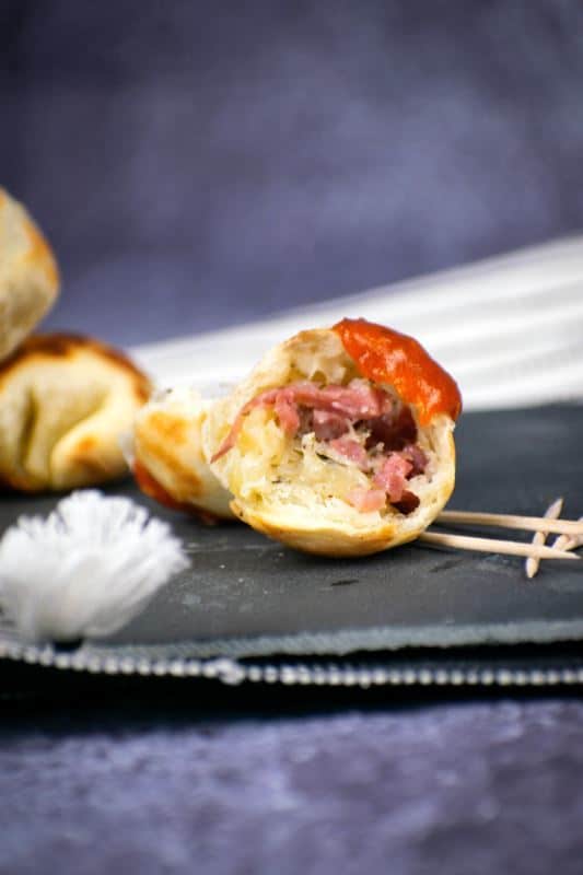 A pizza ball cut in half, ham and cheese on the inside, covered in marinara sauce on a black serving plate.