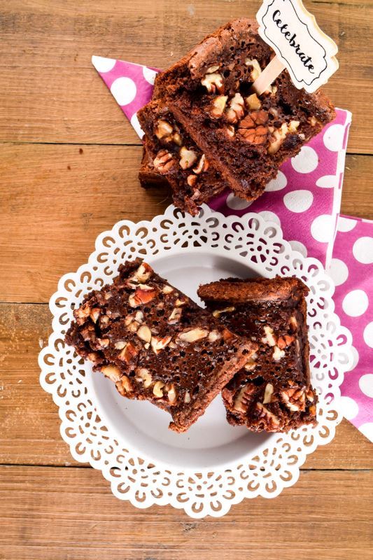 Stacked brownies on a wooden table and polka dot napkins. A popsicle stick in the top brownie with a note saying celebrate.