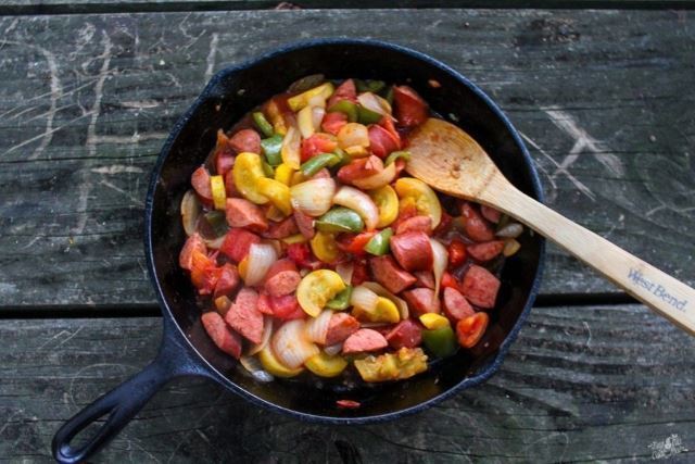 Skillet of sausage and veg with spatula.