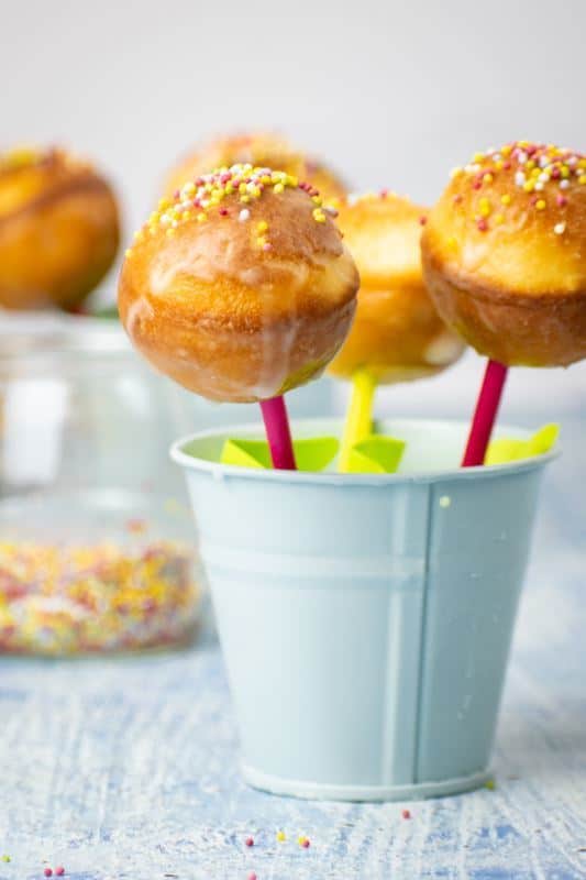 A baby blue pail filled with cake pops, sprinkles in the background.