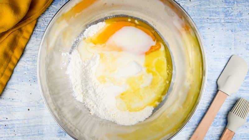 Cake mix, milk, egg and butter in a bowl, spatula and pastry brush on the side.