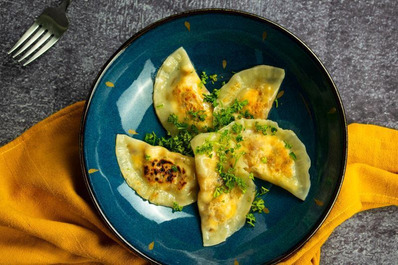 Freshly cooked pierogies on a beautiful blue Portuguese plate, yellow kitchen cloth underneath.