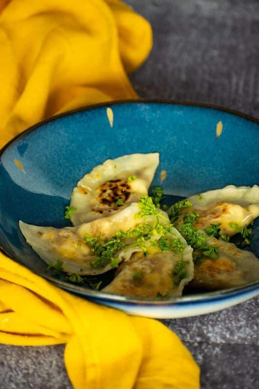 Freshly cooked pierogies on a beautiful blue Portuguese plate, yellow kitchen cloth underneath.