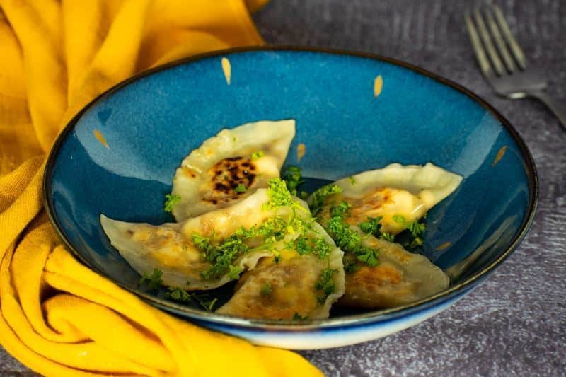 Freshly cooked pierogies on a beautiful blue Portuguese plate, yellow kitchen cloth underneath.