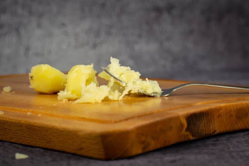 Potatoes mashed with a fork on a cutting board.