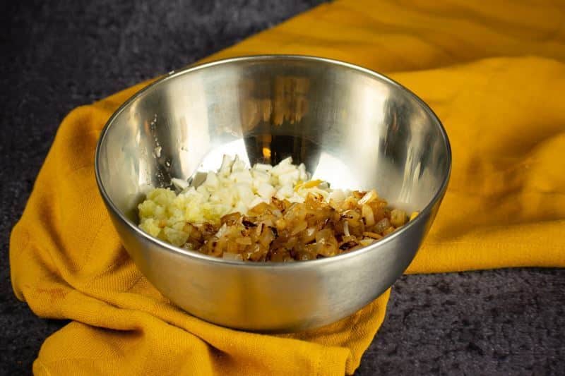 Cheeses, potato and onions in a bowl, yellow dish cloth underneath.