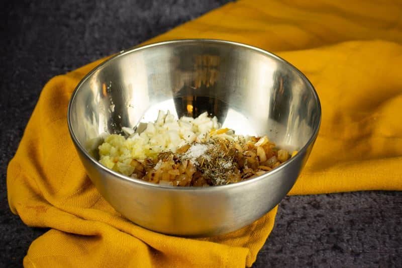 Cheeses, spices, potato and onions in a bowl, yellow dish cloth underneath.