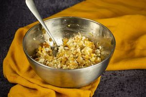 Cheeses, spices, potato and onions in a bowl mixed together, yellow dish cloth underneath.