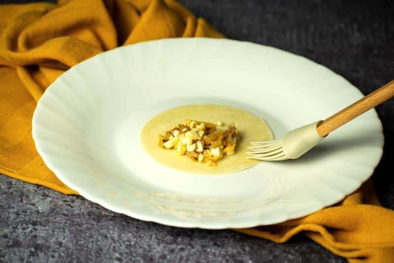 Pierogi disc on a white plate with filling, water being brushed on edges.