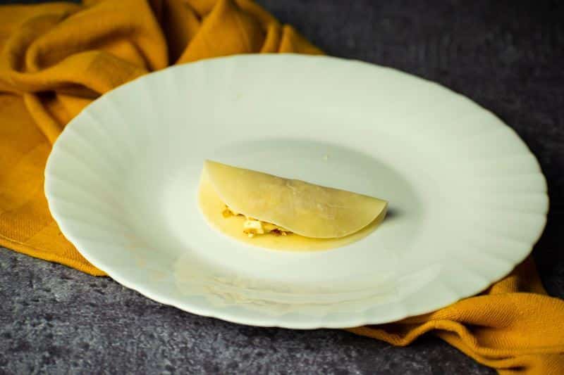 Pierogie disc folded over filling on a white plate.