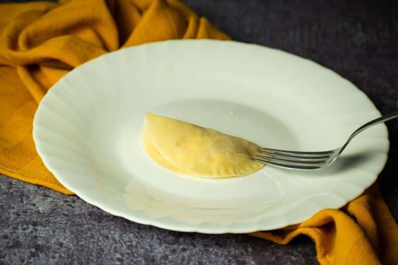 A fork closing up the pierogi edges on a white plate.
