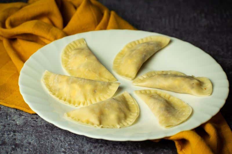 Raw pierogies on a white plate, yellow dish cloth underneath.