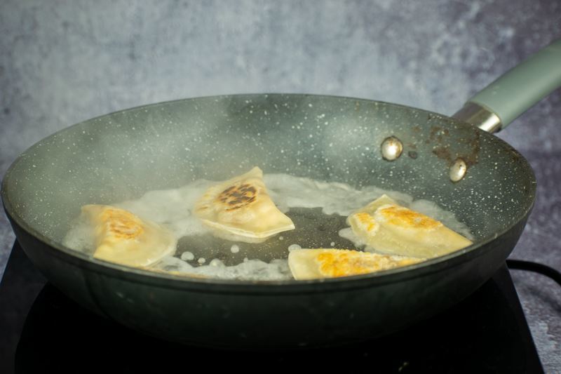 Pierogies cooking in a frying pan.
