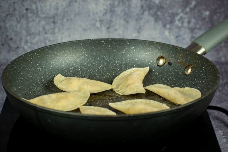 Raw pierogies in a frying pan starting to cook.