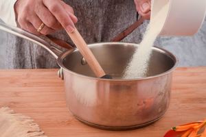 Woman's hand pouring sugar into a pot and mixing with water.