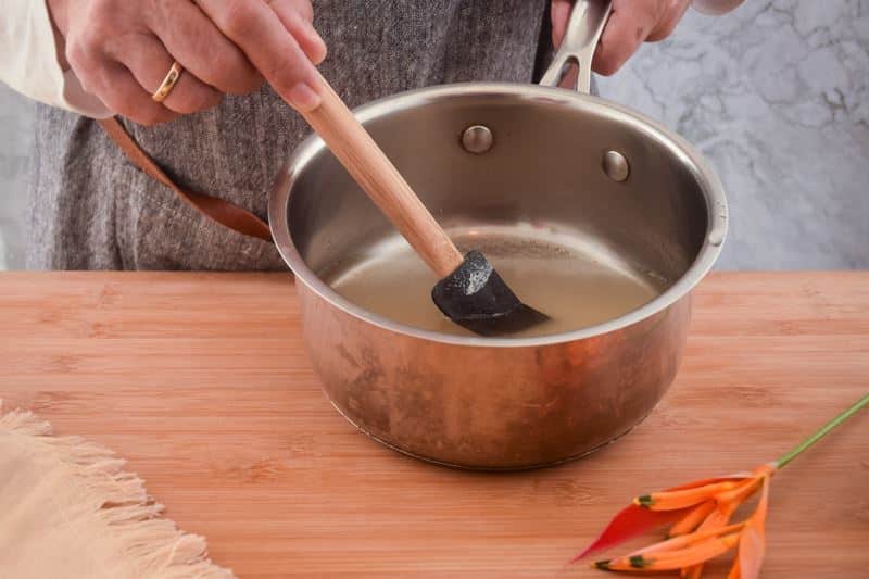 How to Make Simple Syrup Step 4 Woman's hand mixing a sugar and water mixture in a pot.