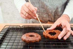 A small chocolate cake sliced in half, woman poking holes into them with a wooden skewer.