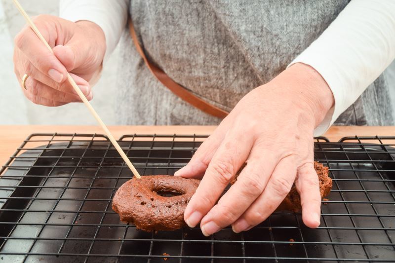 A small chocolate cake sliced in half, woman poking holes into them with a wooden skewer.