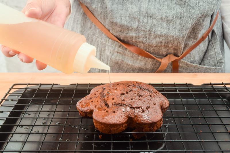 Woman pouring syrup into chocolate cake with holes in it.
