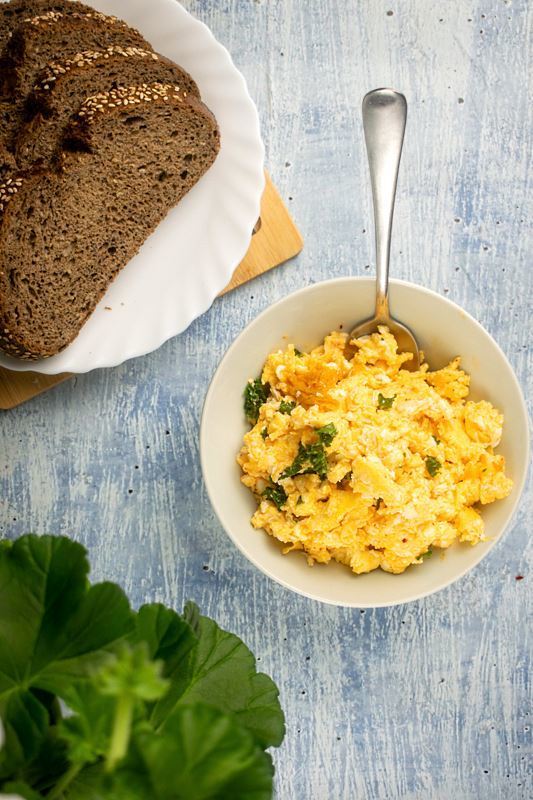 A pot of scrambled eggs with kimchi and kale on counter, a plate of sliced bread on the side.