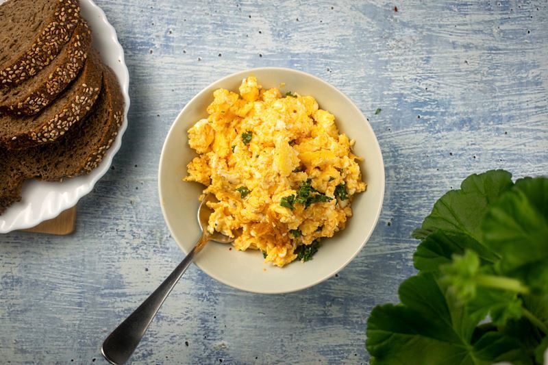 A pot of scrambled eggs with kimchi and kale on counter, a plate of sliced brown bread on the side.