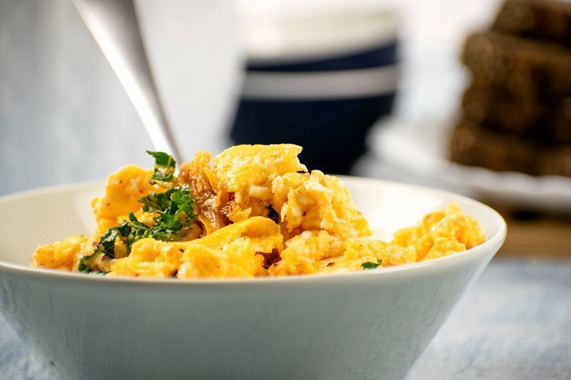 A pot of scrambled eggs with kimchi and kale with a fork in it.