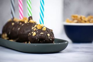Banana cake pops upside down on a black tray with colorful, striped treat sticks.