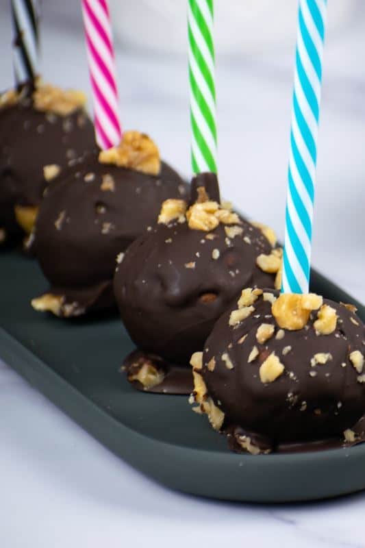 Banana cake pops upside down on a black tray with colorful, striped treat sticks.