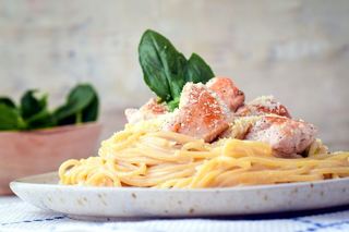 Electric Skillet Spaghetti chicken alfredo on a white speckled plate, garnished with basil leaves.