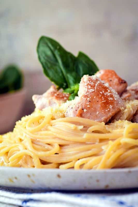 Electric Skillet Spaghetti chicken alfredo on a white speckled plate, garnished with basil leaves.