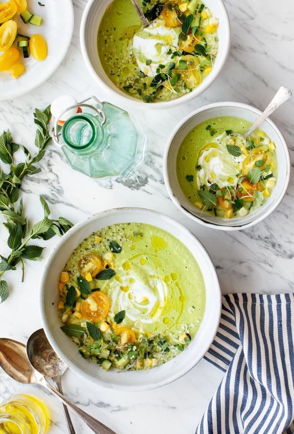 Green cucumber tomatillo gazpacho in 3 white bowls on a marble background.